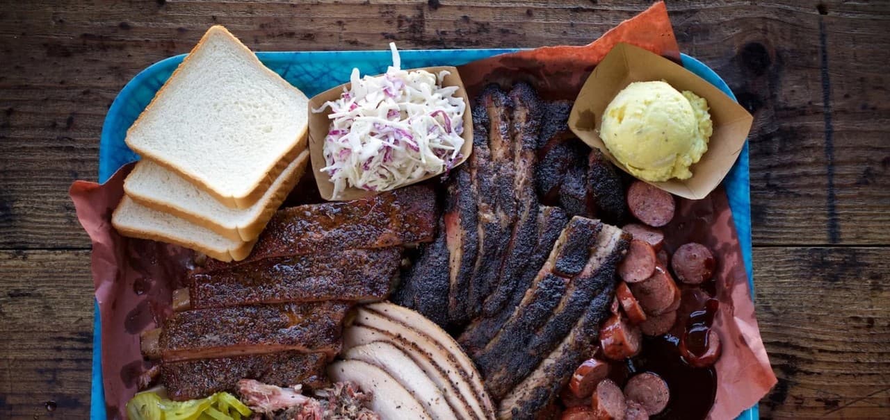 Overhead view of a Franklin Barbecue tray with sliced brisket, sausage, bread, and sides