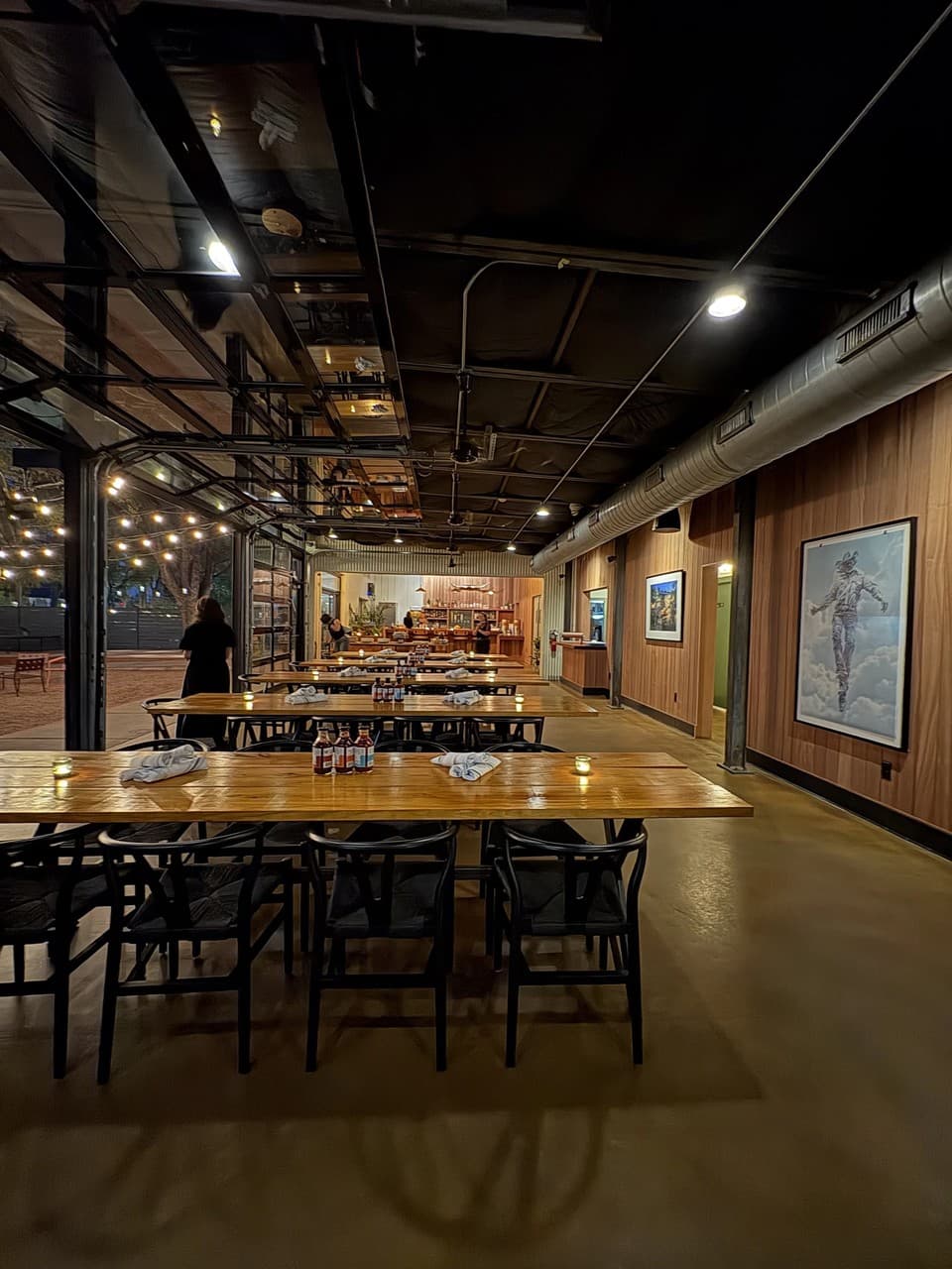 A warmly lit modern restaurant dining hall with long communal tables