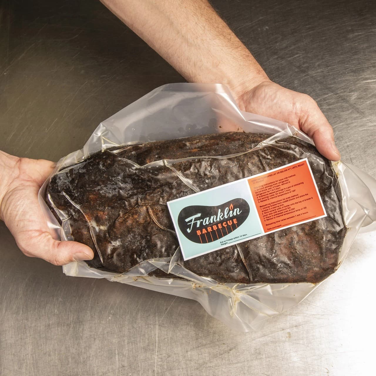 Hands holding a vacuum-sealed smoked brisket ready for nationwide shipping
