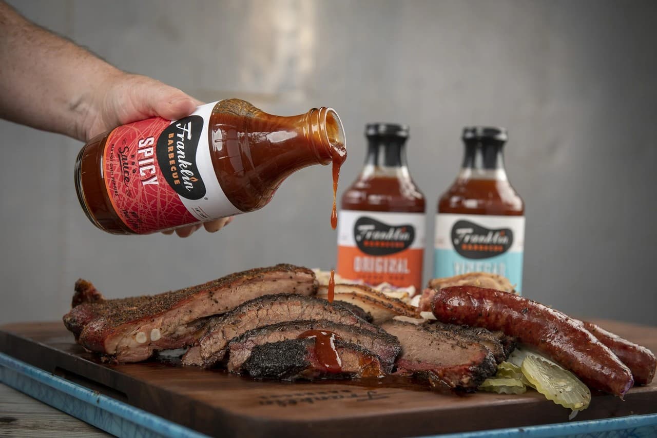 Close-up of barbecue brisket, sausage, and sauce bottles on a rustic table